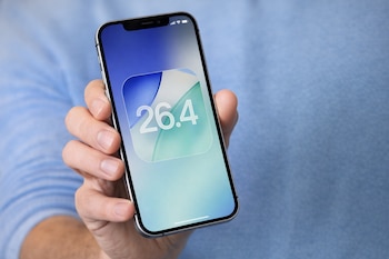 Mano sosteniendo un iPhone con la pantalla mostrando el número 26.4 en fondo azul y verde.