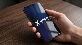 Primer plano de una mano sosteniendo un smartphone negro con el logo blanco de Xuper TV en la pantalla, sobre una superficie de madera oscura.
