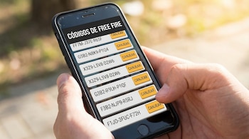 Primer plano de una persona sosteniendo un smartphone que muestra una pantalla con una lista de códigos de Free Fire y botones de 'Canjear'.