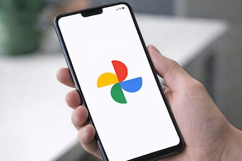 Primer plano de una mano sosteniendo un smartphone negro que muestra el logo multicolor de Google Fotos en su pantalla blanca.